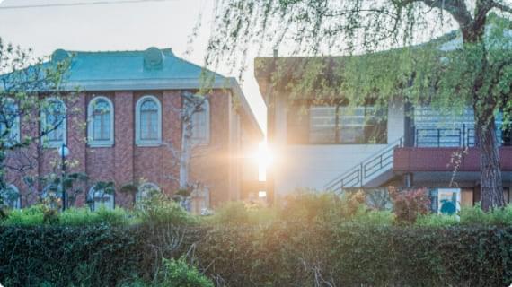 A historical red brick building bathed in the sunset, with landscaped plants in front.