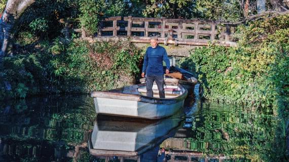 A boatman guiding a small boat along the canal. Wearing a traditional hat, he uses a long pole to steer the boat.