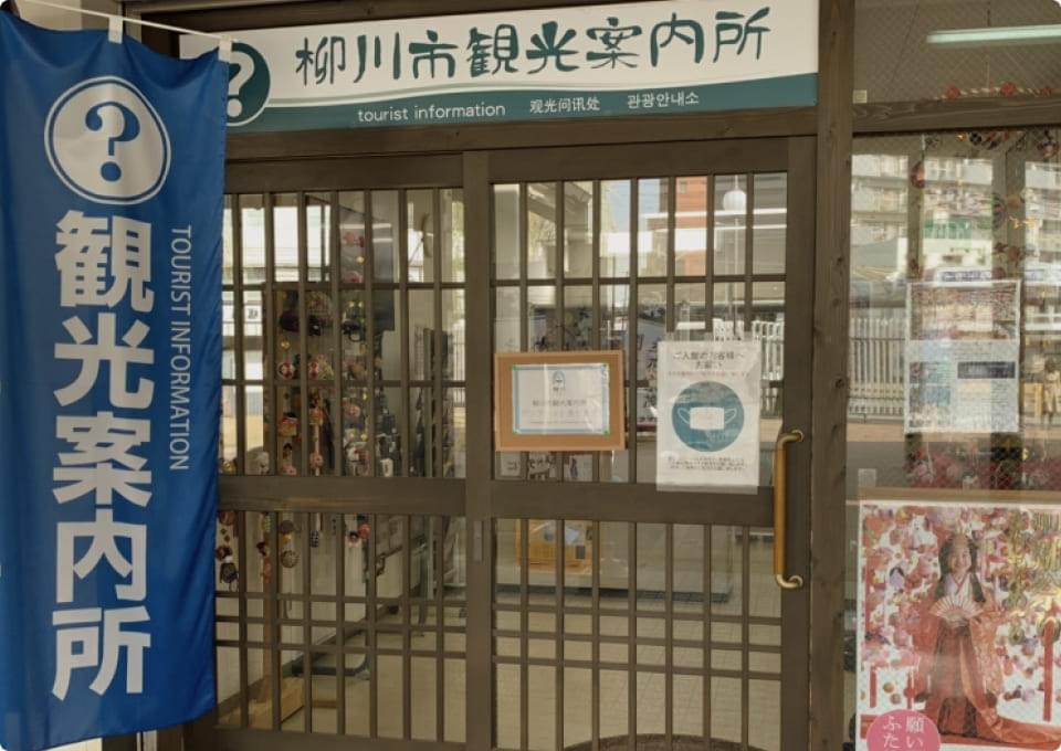 The entrance to Yanagawa City Tourist Information Center. There is a multilingual sign and blue tourist information flags.