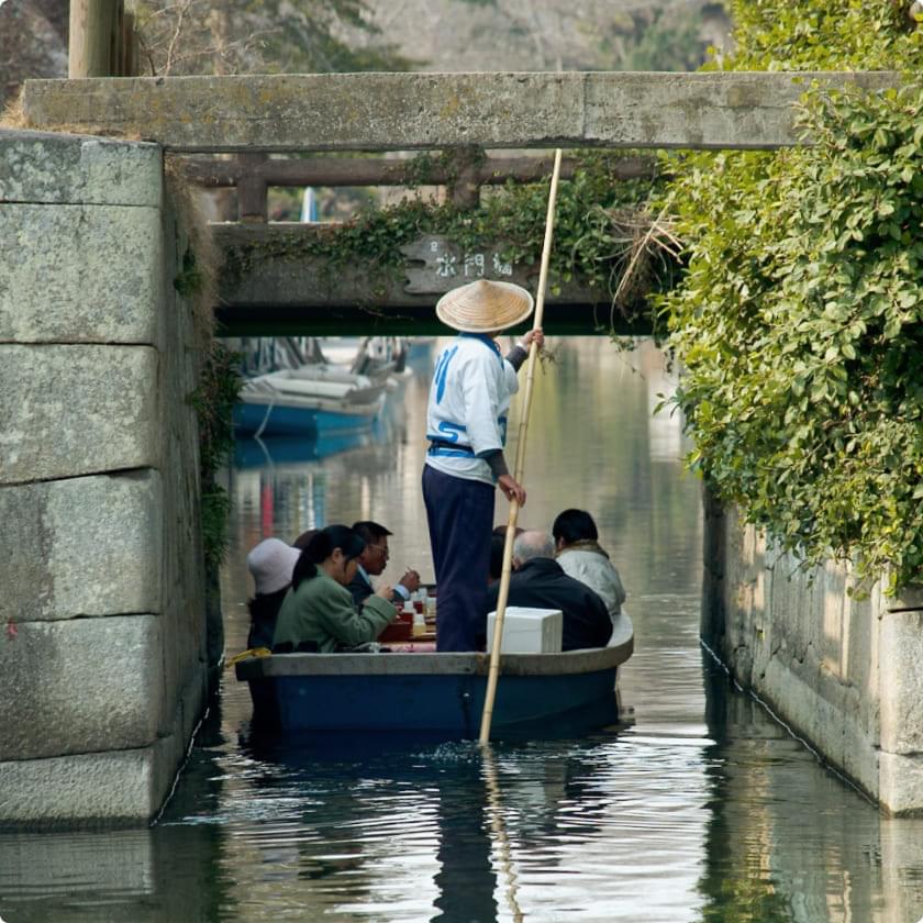 石造りのアーチをくぐる観光船。船頭が竿を操り、乗客が川下りを楽しんでいる様子。